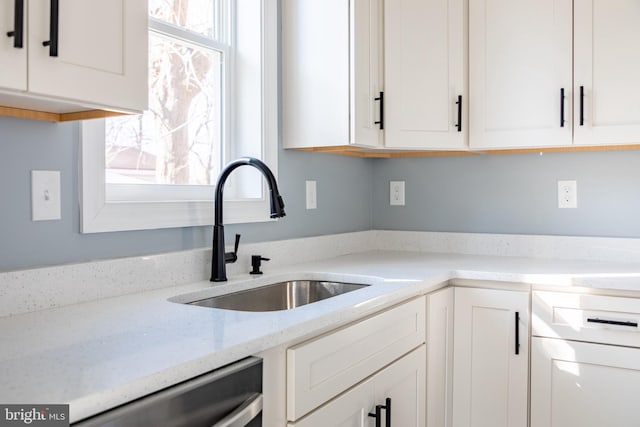 kitchen with dishwasher, white cabinetry, light stone counters, and a sink