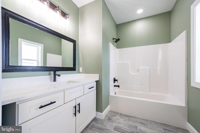 bathroom with washtub / shower combination, baseboards, wood finish floors, and vanity