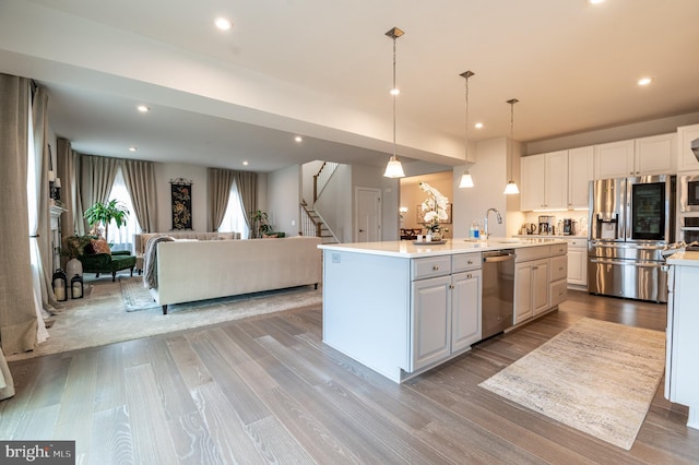 kitchen featuring white cabinets, an island with sink, stainless steel appliances, and hanging light fixtures