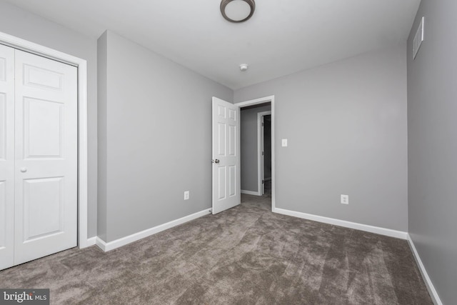 unfurnished bedroom with dark carpet and a closet