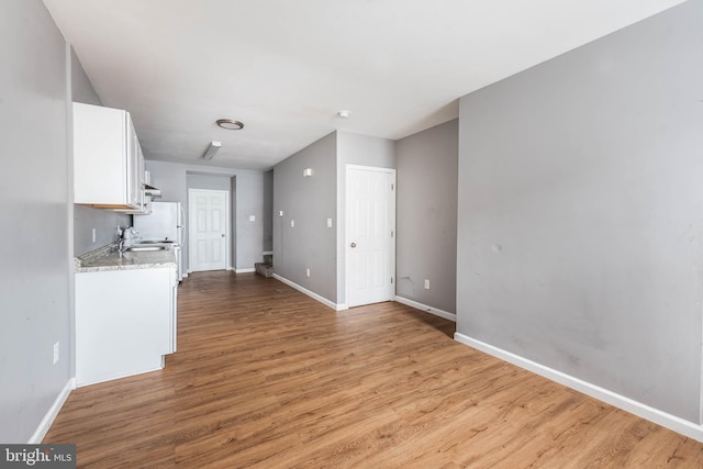 kitchen with sink, light hardwood / wood-style flooring, white cabinetry, light stone countertops, and white fridge