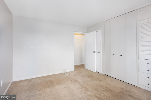 unfurnished bedroom with a closet, light colored carpet, and baseboards