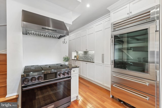 kitchen featuring extractor fan, white cabinets, stainless steel gas range oven, and light hardwood / wood-style floors