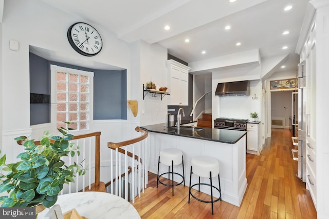 kitchen with light hardwood / wood-style flooring, wall chimney range hood, sink, white cabinetry, and kitchen peninsula