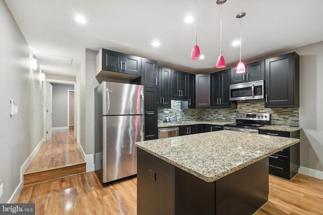 kitchen with stainless steel appliances, a kitchen island, light stone counters, and decorative light fixtures