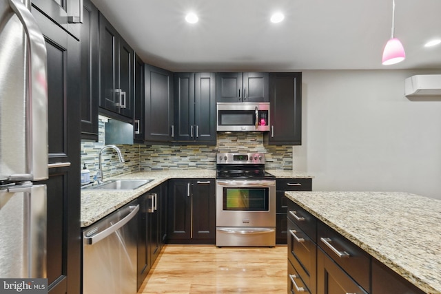 kitchen with appliances with stainless steel finishes, light stone counters, pendant lighting, sink, and light wood-type flooring