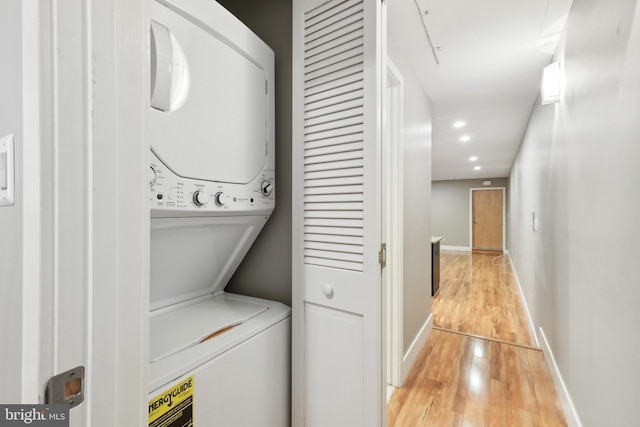 clothes washing area featuring wood-type flooring and stacked washer and clothes dryer