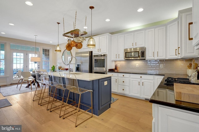 kitchen featuring appliances with stainless steel finishes, white cabinetry, a kitchen island with sink, and decorative light fixtures