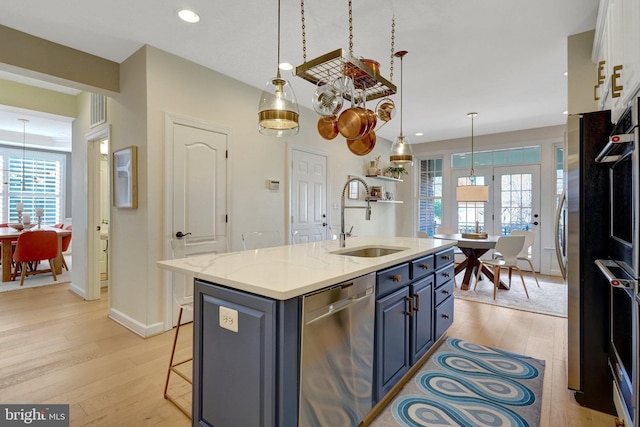 kitchen with a center island with sink, sink, pendant lighting, stainless steel appliances, and light stone countertops