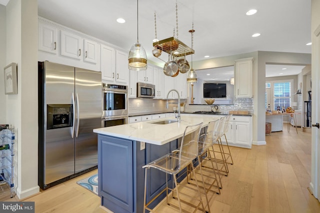 kitchen with appliances with stainless steel finishes, sink, a breakfast bar, light stone counters, and white cabinets