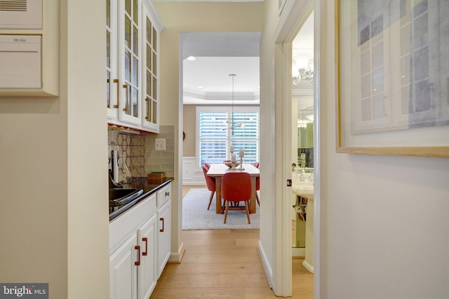 interior space featuring white cabinets, light hardwood / wood-style flooring, tasteful backsplash, and decorative light fixtures