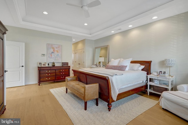 bedroom featuring a tray ceiling, ornamental molding, light wood-type flooring, and ceiling fan