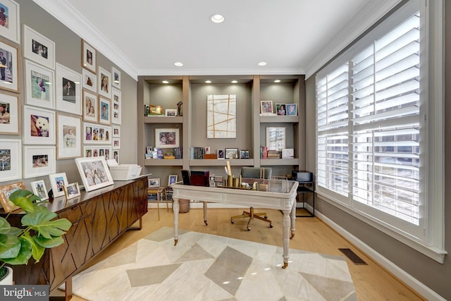 home office featuring light wood-type flooring, built in shelves, and ornamental molding