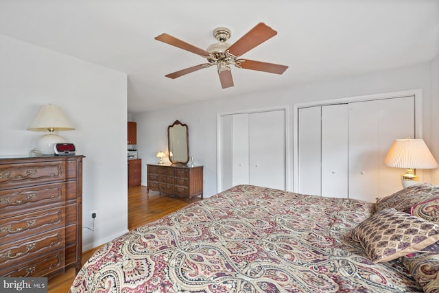 bedroom featuring ceiling fan, light hardwood / wood-style floors, and multiple closets