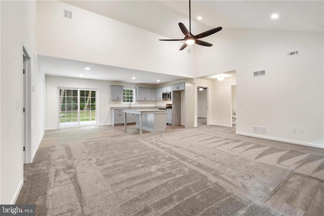 unfurnished living room with high vaulted ceiling, light colored carpet, and ceiling fan