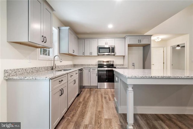 kitchen with stainless steel appliances, sink, light stone counters, and light hardwood / wood-style floors