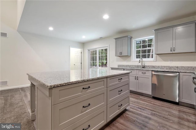 kitchen featuring gray cabinetry, a center island, light stone counters, wood-type flooring, and stainless steel dishwasher