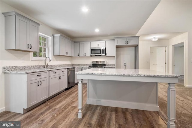 kitchen featuring light stone counters, a kitchen island, wood-type flooring, and appliances with stainless steel finishes