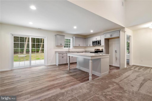 kitchen featuring a breakfast bar, a center island, appliances with stainless steel finishes, gray cabinets, and light stone countertops