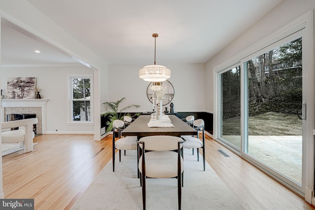 dining room with light wood finished floors, a fireplace, visible vents, and baseboards