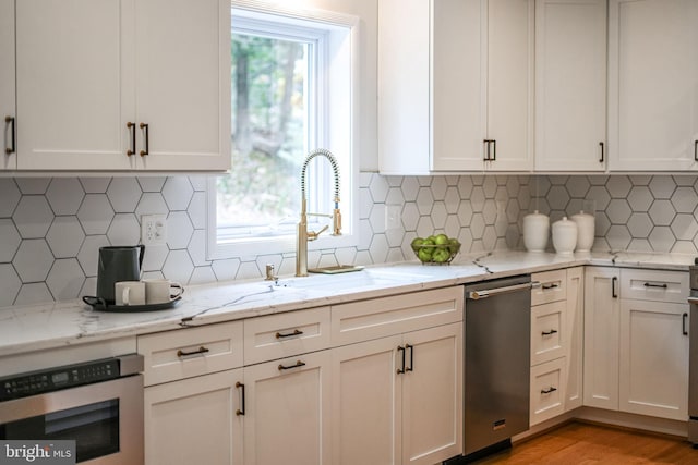 kitchen with light stone counters, light wood finished floors, appliances with stainless steel finishes, white cabinets, and a sink