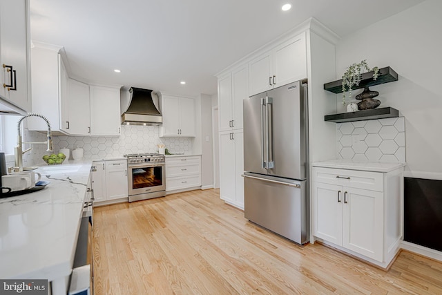 kitchen with light stone counters, white cabinets, high quality appliances, light wood-type flooring, and premium range hood