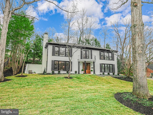 view of front of home with a balcony, a chimney, a front lawn, and brick siding