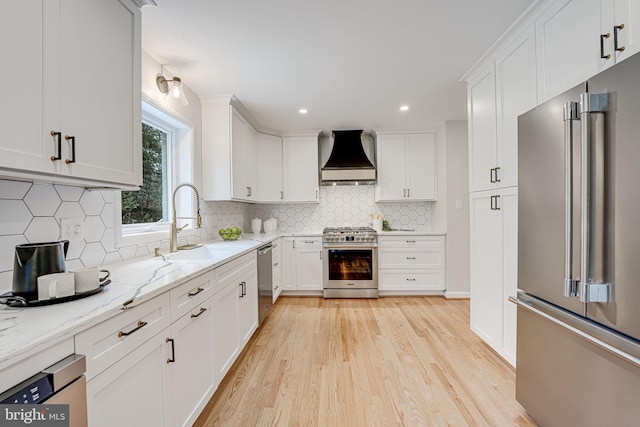 kitchen featuring premium appliances, white cabinetry, light wood-type flooring, light stone countertops, and custom range hood