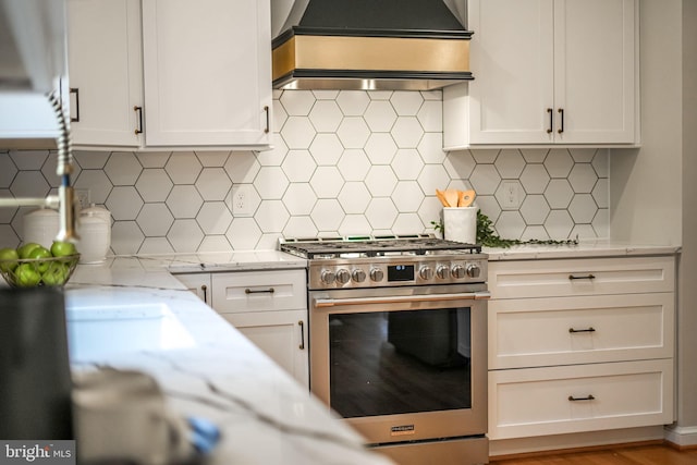 kitchen with light stone countertops, premium range hood, high end range, and white cabinetry