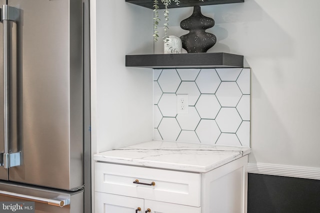 room details featuring light stone counters, high end refrigerator, decorative backsplash, white cabinets, and baseboards