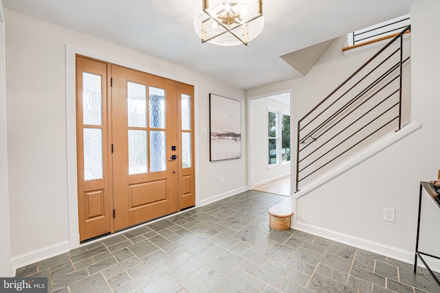 foyer with a notable chandelier, baseboards, stairway, and stone tile flooring