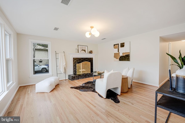 living room featuring light wood finished floors, baseboards, visible vents, and a fireplace with raised hearth