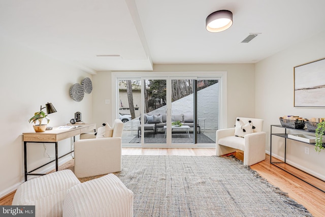 sitting room with beam ceiling, light wood-type flooring, visible vents, and baseboards