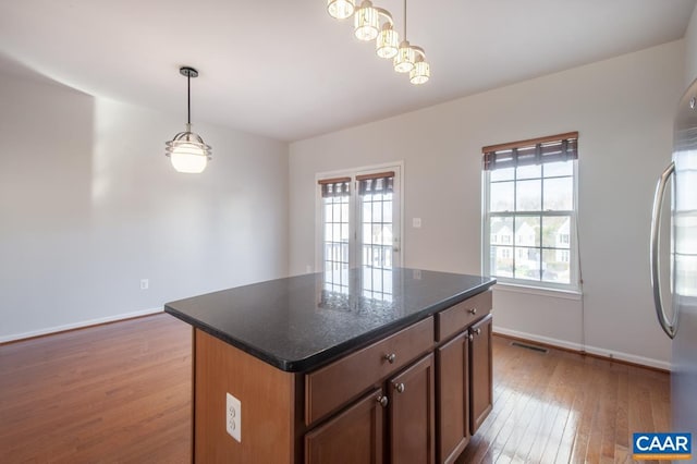 kitchen with hanging light fixtures, dark stone countertops, light wood-type flooring, stainless steel fridge, and a kitchen island