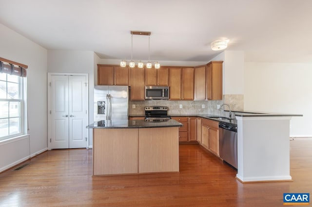 kitchen with appliances with stainless steel finishes, pendant lighting, sink, backsplash, and a center island