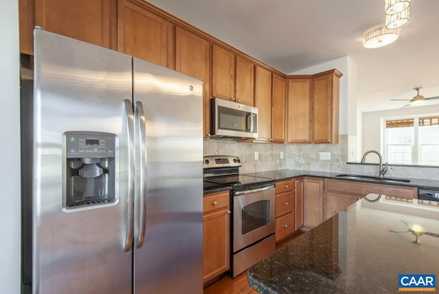 kitchen with sink, decorative light fixtures, dark stone countertops, stainless steel appliances, and decorative backsplash