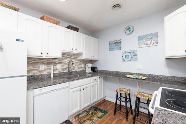 kitchen featuring sink, white appliances, white cabinetry, dark stone countertops, and backsplash