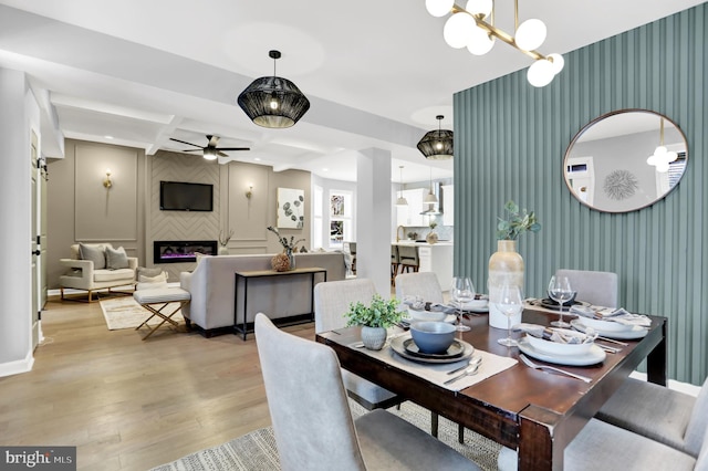 dining space featuring ceiling fan with notable chandelier, a fireplace, light wood-type flooring, coffered ceiling, and beam ceiling