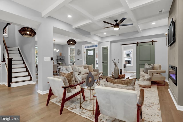 living room with coffered ceiling, beamed ceiling, a barn door, and light wood-type flooring