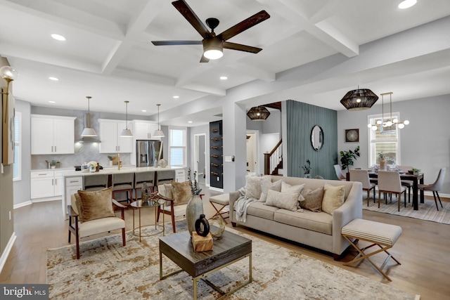 living room featuring coffered ceiling, ceiling fan with notable chandelier, beam ceiling, and light hardwood / wood-style flooring