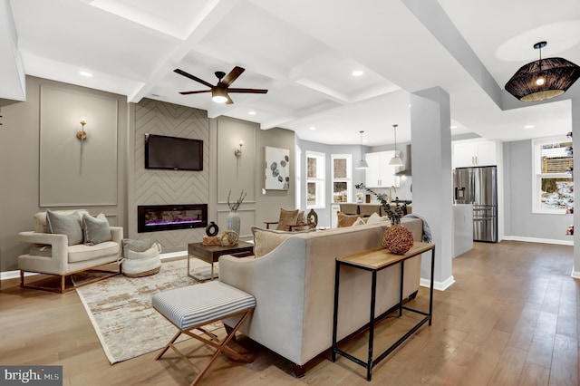 living room with light hardwood / wood-style flooring, ceiling fan, beam ceiling, coffered ceiling, and a large fireplace