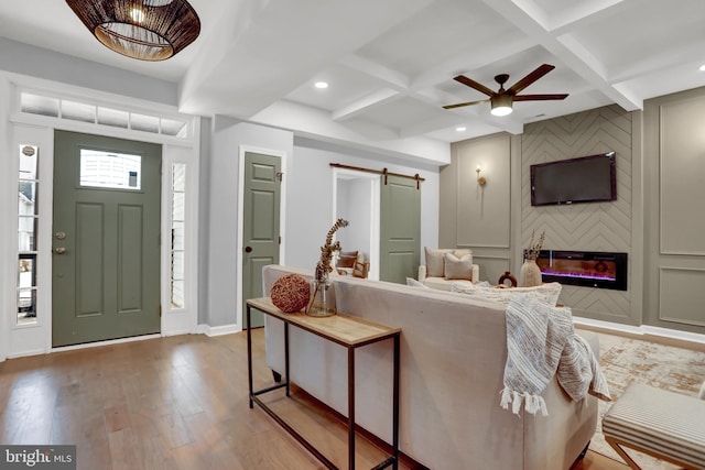 living room featuring coffered ceiling, a large fireplace, a barn door, beamed ceiling, and light wood-type flooring