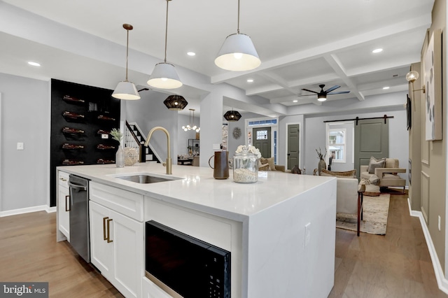 kitchen with sink, hanging light fixtures, an island with sink, a barn door, and white cabinets