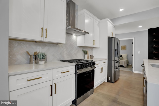 kitchen with white cabinetry, decorative backsplash, light hardwood / wood-style floors, stainless steel appliances, and wall chimney range hood