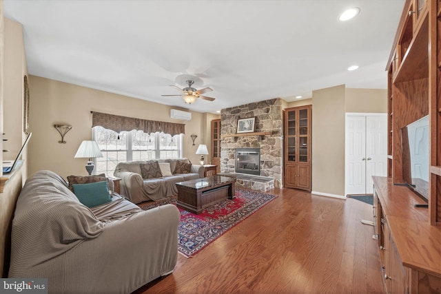 living area with ceiling fan, a stone fireplace, recessed lighting, wood finished floors, and a wall mounted AC