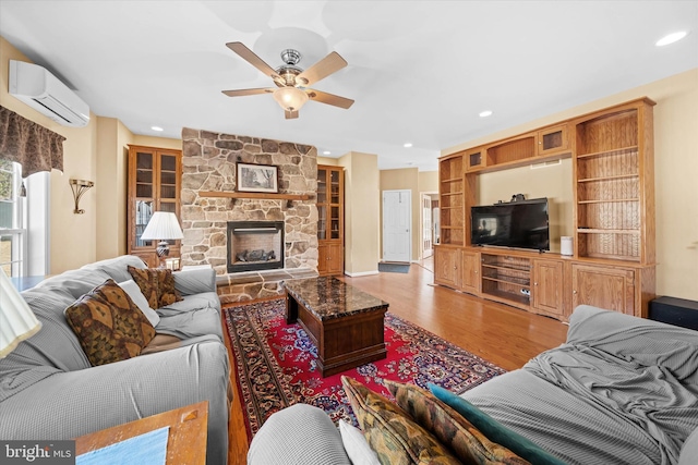 living area with ceiling fan, a wall mounted air conditioner, light wood-type flooring, a fireplace, and recessed lighting