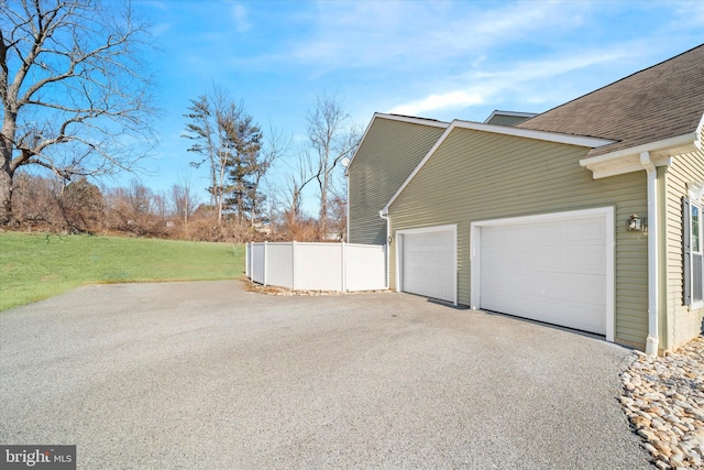 view of side of property featuring a garage, a shingled roof, fence, and a yard