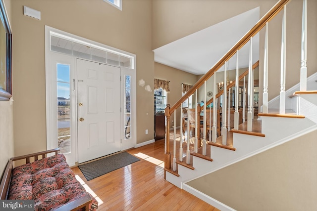 entryway with a towering ceiling, hardwood / wood-style flooring, stairs, and baseboards