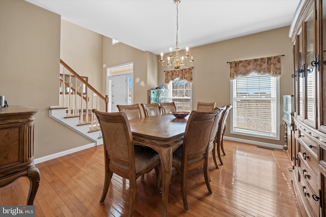 dining area featuring light wood finished floors, baseboards, stairway, and a notable chandelier