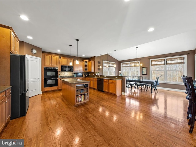 kitchen with black appliances, wood finished floors, a peninsula, brown cabinetry, and lofted ceiling